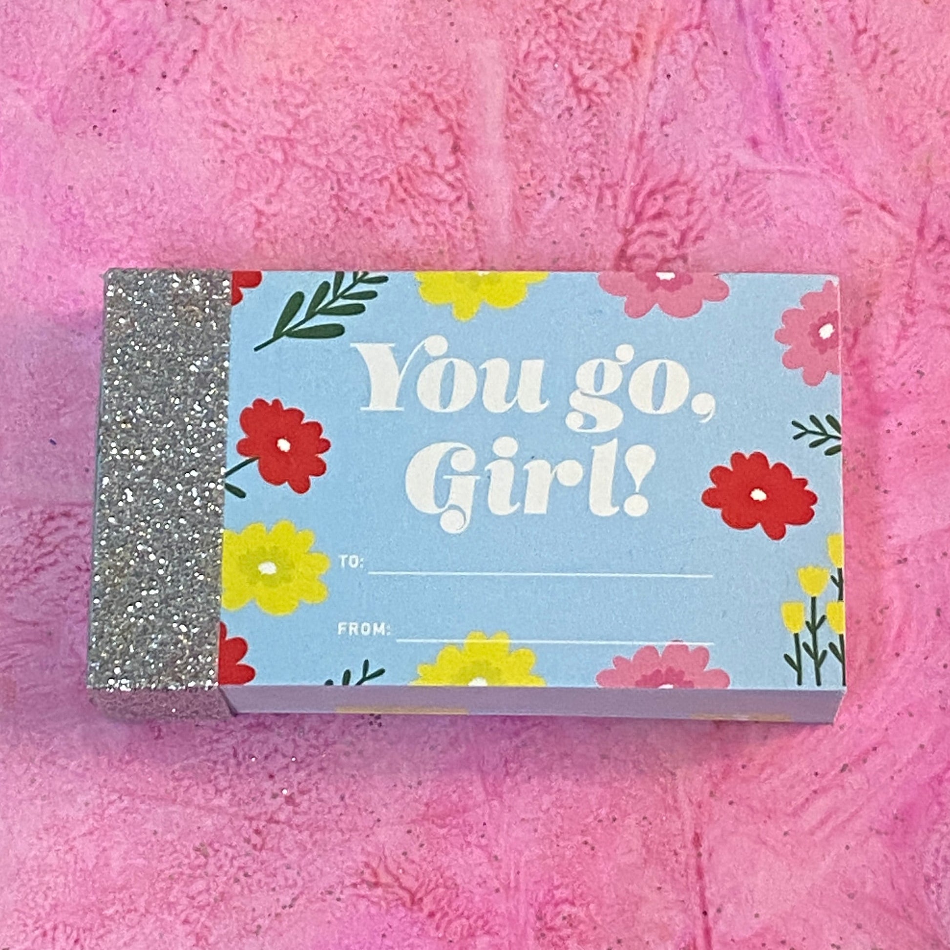 Flipbook with 'You go, Girl!' cover with text and flowers and a glittery book spine. Flipbook lies on a pink textured background